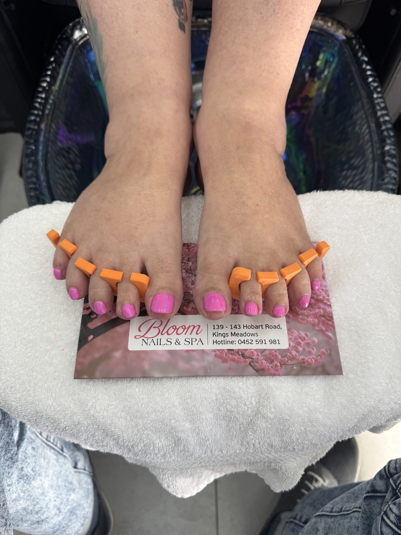 A fresh pink pedicure with toe separators, resting on a Bloom business card